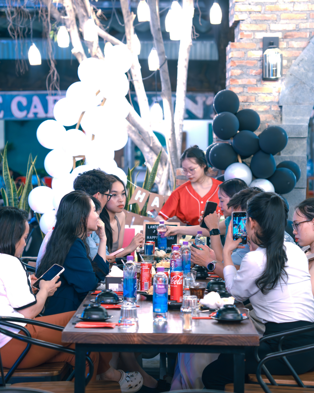 Group of people sitting around a table at Lantern Garden with drinks and phones in an outdoor setting.